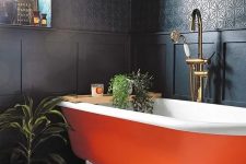 20 a refined moody bathroom with black walls and paneling, an orange clawfoot bathtub, potted greenery and candles is wow