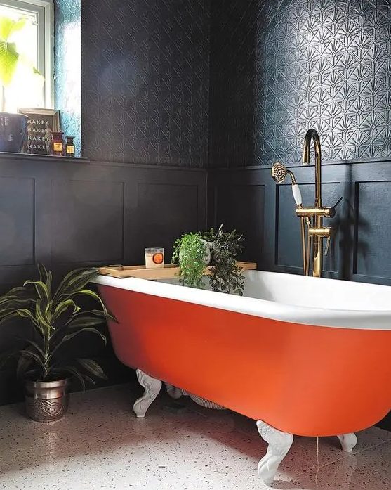 a refined moody bathroom with black walls and paneling, an orange clawfoot bathtub, potted greenery and candles is wow