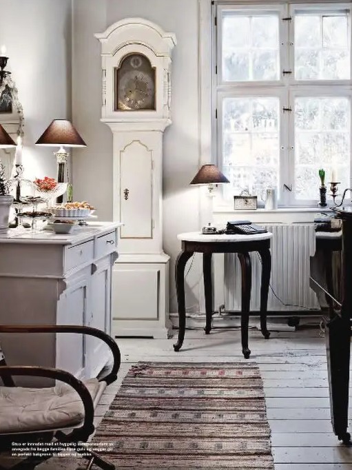 a Scandinavian kitchen with a white and gold grandfather's clock and whitewashed furniture, some dark-stained pieces for a contrast