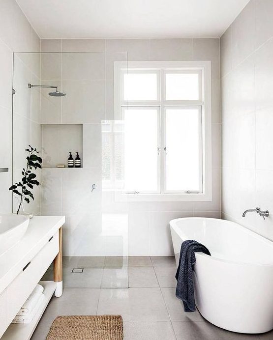 a refreshing Scandinavian bathroom with white walls, an oval tub, a long white vanity and a jute rug
