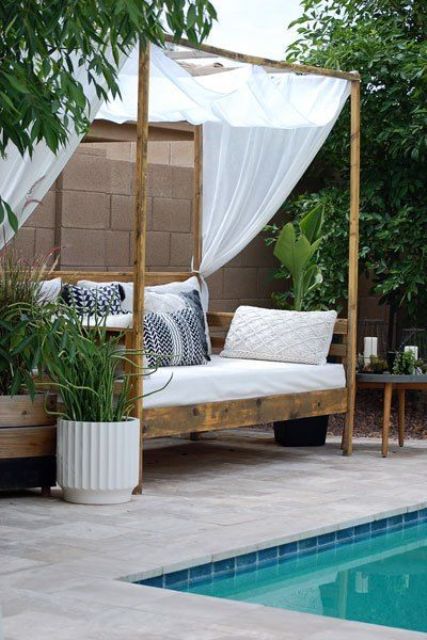 a simple stained canopy outdoor daybed with an arrangement of pillows, a canopy to protect from excessive sunlight and greenery around