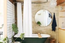 23 a stylish bathroom with white tiles and brick walls, a dark green clawfoot bathtub, a round mirror, a wooden vanity and potted plants