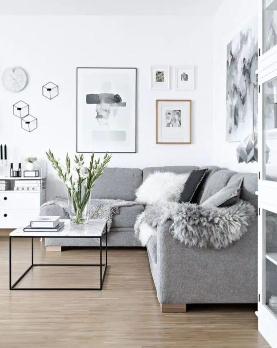 a Scandinavian living room done in white and greys, faux fur and pillows add coziness to the space
