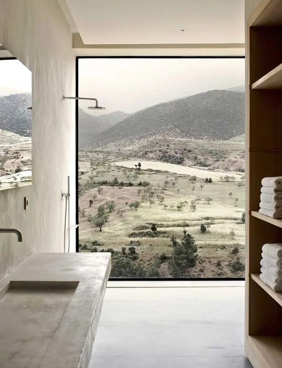 a minimalist bathroom done with concrete, with a glazed wall, a large storage unit, a wall-mounted concrete sink and a beautiful view