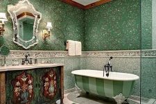 24 a unique green bathroom with botanical wallpaper, green tiles on the walls, a green striped clawfoot bathtub, an inlay vanity and a crystal chandelier