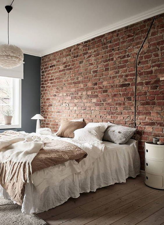 an exposed red brick wall as a statement in the room, neutral furniture, a fluffy pendant lamp and a cool nightstand