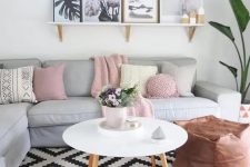 25 a Scandinavian living room with a grey sectional, pastel and neutral pillows, a ledge gallery wall, a potted plant and a copper leather pouf