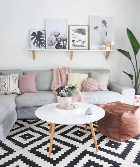 a Scandinavian living room with a grey sectional, pastel and neutral pillows, a ledge gallery wall, a potted plant and a copper leather pouf