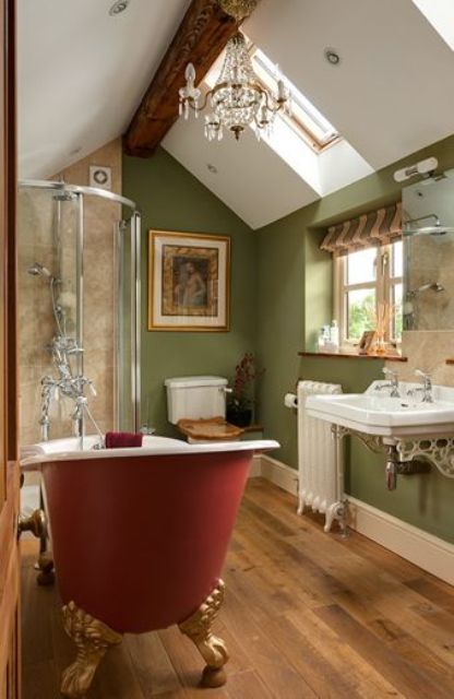 a vintage attic bathroom with green walls, a crystal chandelier, a burgundy clawfoot bathtub, a wall-mounted sink, some art and a striped curtain