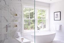 26 a neutral bathroom clad with white marble tiles, an oval tub by the window, a shower space and blank space for a more luxurious look