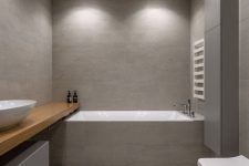 27 a minimalist bathroom clad with grey large scale tiles, with a floating shelf vanity, a bathtub clad with tiles and a toilet