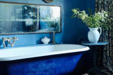 27 a vintage-inspired bathroom with blue walls and an electric blue bathtub, a bold printed rug, a vintage mirror, greenery and printed curtains