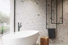 28 a minimalist bathroom clad with grey terrazzo, with a platform and a bathtub on top, black radiators and a glazed wall