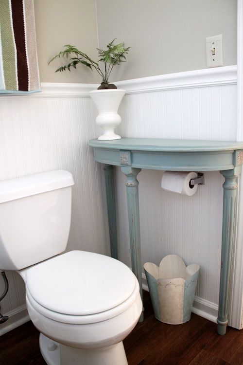 a small powder room with a white toilet, a light blue half table, a potted plant and a metal bucket is a chic idea