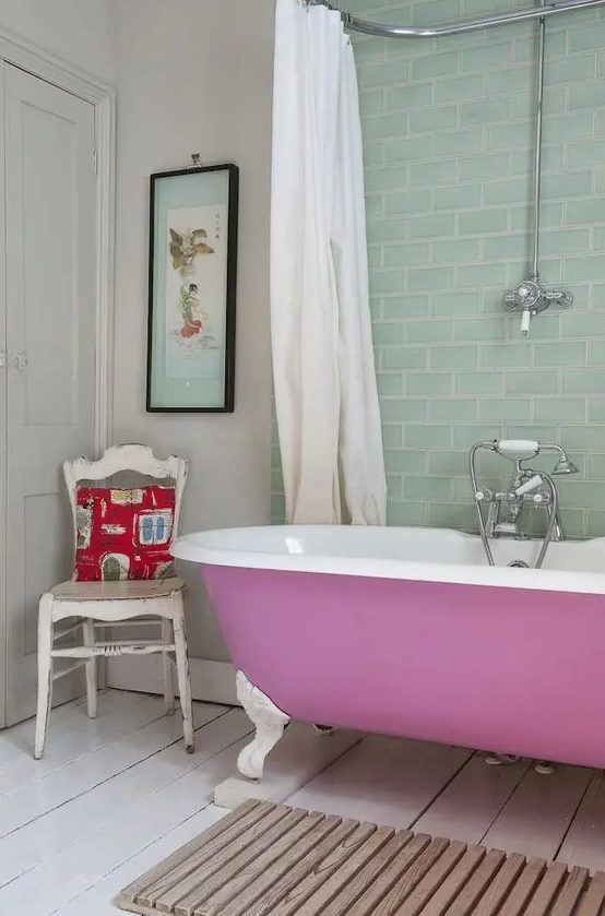 an eclectic bathroom with white walls and an aqua tile backsplash, a mauve clawfoot tub, a wooden mat and a shabby chic chair