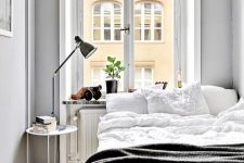 29 a small Nordic bedroom with a bed, a nighstand with a lamp, potted greenery and grey walls