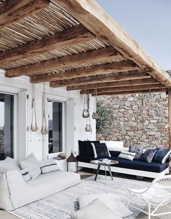 a beautiful terrace with a roof, a low white daybed with striped pillows, a white daybed with a navy mattress and pillows, pendant lamps
