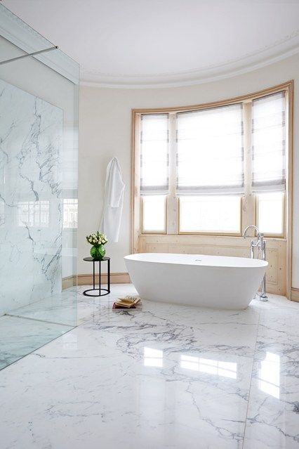 a fantastic idea of a bathroom clad with white marble tiles, an oval tub, a glass-enclosed shower space and much negative space
