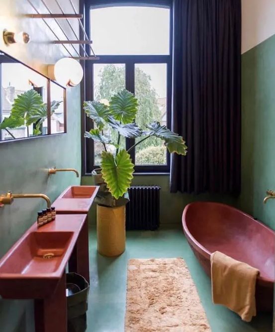 a green maximalist bathroom with red free-standing sinks, a red oval bathtub, a neutral rug, potted plants and a mirror, black curtains