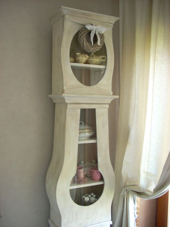 a neutral grandfather clock fully renovated into a storage unit with glass doors and a wreath with a bow