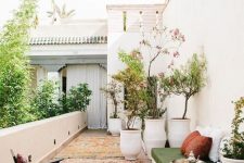 31 a beautiful Morocco-inspired balcony with oversized potted trees and blooms, a low daybed with a mattress and pillows, Moroccan rugs and a dark stained chair