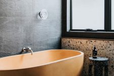 31 a moody minimalist bathroom clad with large scale tiles, terrazzo in neutrals and black, a beautiful and textural orange bathtub