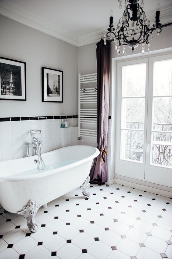 a refined Parisian bathroom with a clawfoot bathtub, a crystal chandelier, purple curtains, a gallery wall and negative space to enjoy the  airy feel