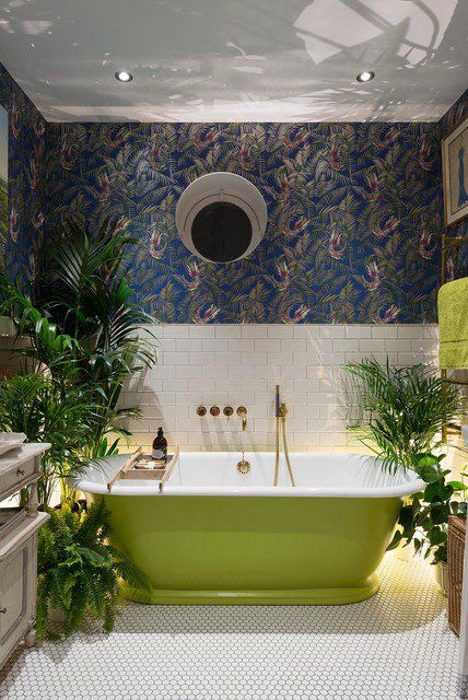 a stylish bathroom with botanical wallpaper, white subway and penny tiles, a neon green modenr tub, potted greenery and a vintage vanity