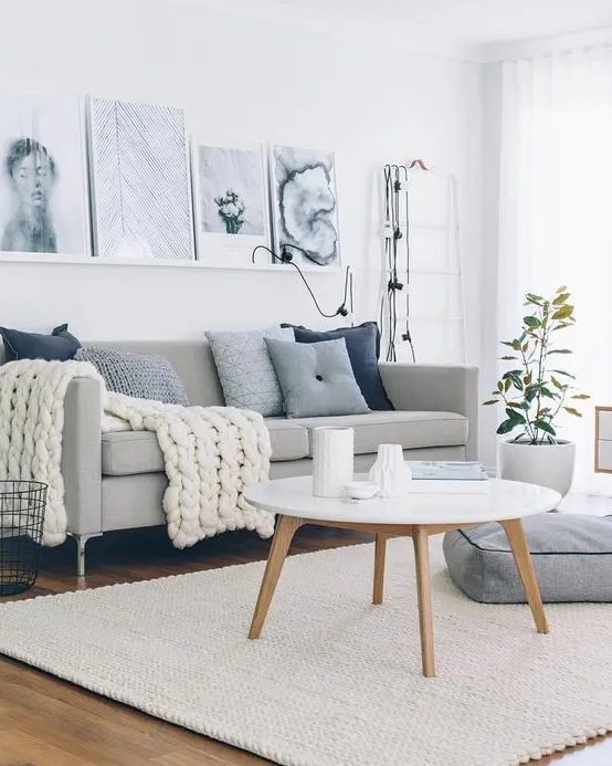 a welcoming Scandinavian living room with a grey sofa, blue pillows, a ledge with black and white artworks, a round table and a cushion on the floor