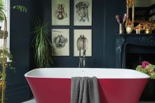 36 a vintage moody bathroom with black walls, a non-working fireplace, a mirror in a gilded frame and a modern burgundy bathtub that makes a statement