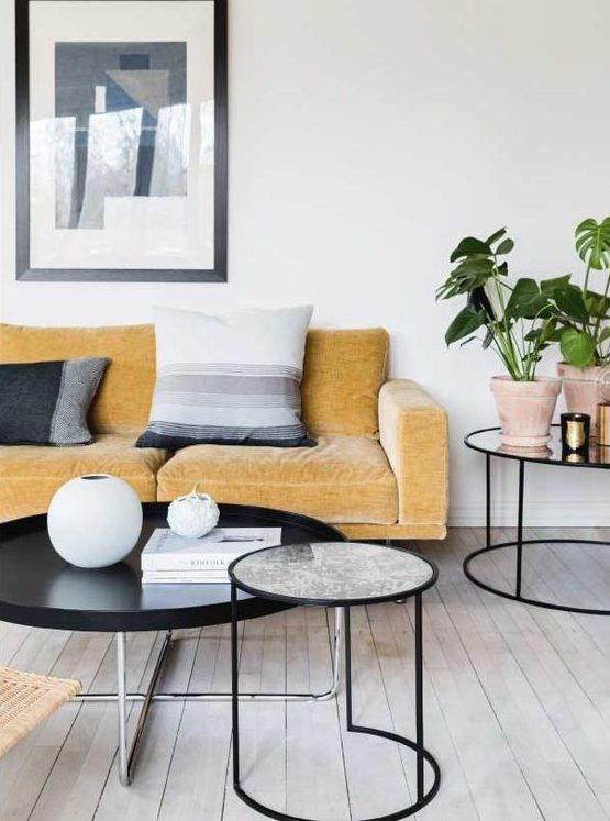 a Nordic living room with a yellow sofa and graphic pillows, round tables, potted plants and graphic art