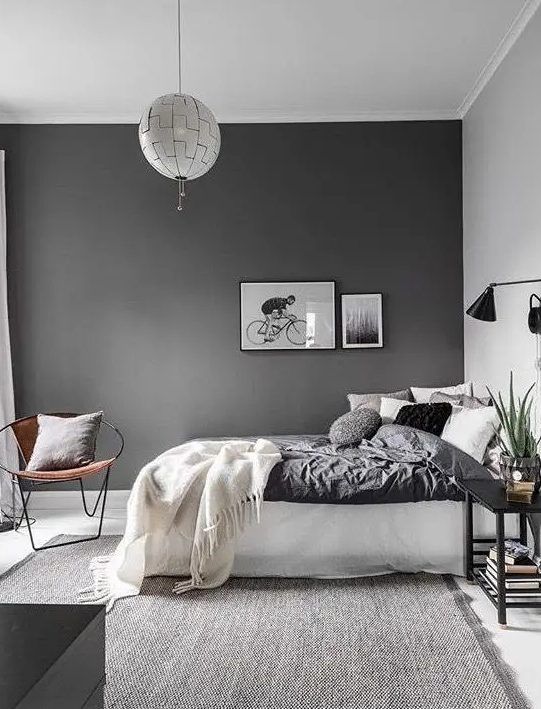 a Scandinavian bedroom with a slate grey accent wall, a white bed with lots of pillows, black sconces and a nightstand