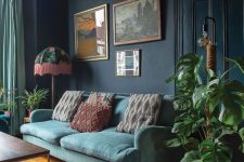 a Victorian living room with navy walls, an aqua sofa with printed pillows, a gallery wlal, potted plants and printed pillows