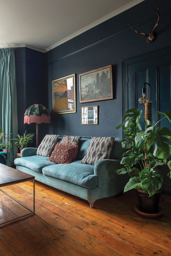 a Victorian living room with navy walls, an aqua sofa with printed pillows, a gallery wlal, potted plants and printed pillows