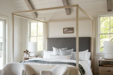 a beautiful and cozy neutral bedroom with shiplap on the ceiling, a frame bed with neutral bedding, light-stained nightstands and creamy chairs at the foot of the bed