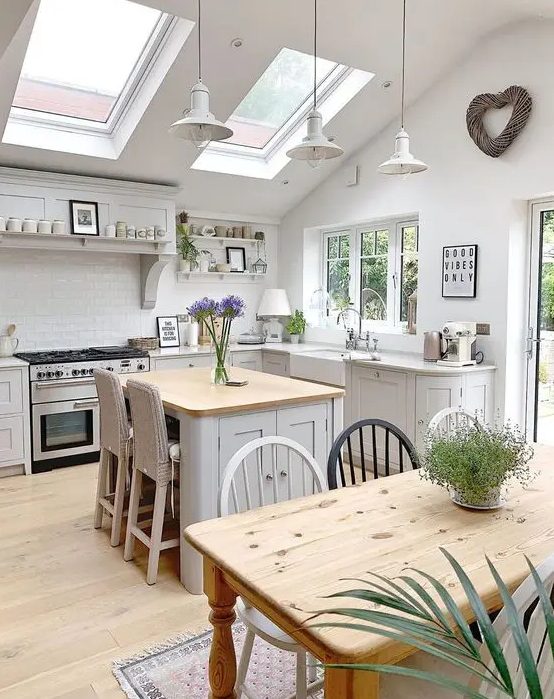 a beautiful attic cottage kitchen with shaker style cabinets, skylights, pendant lamps and a small kitchen island with woven stools
