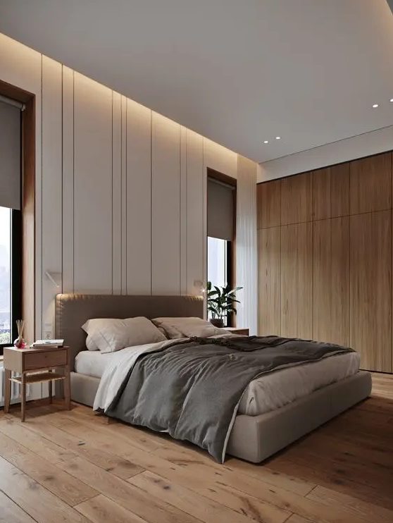 a beautiful contemporary bedroom with built in lights, a grey upholstered bed, grey bedding and curtains, wooden nightstands and a sleek storage unit