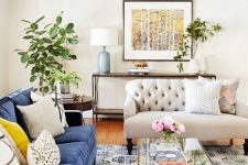 a beautiful living room with a printed rug, a blue sofa, neutral and printed pillows, a creamy sofa, greenery and a gold chandelier