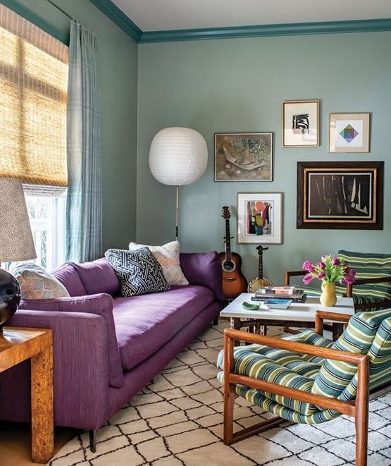 a beautiful living room with light green walls, a purple sofa, striped chairs, a pretty gallery wall and a chic coffee table