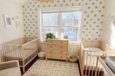 a beautiful neutral boho twin nursery with wooden cribs and a changing table and a dresser, an accent wall, a woven pendant lamp and a jute pouf