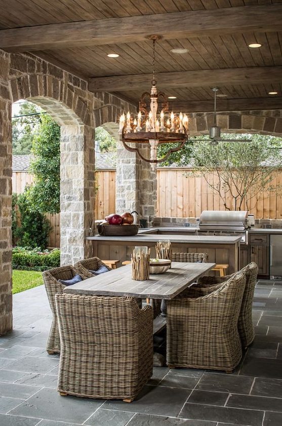 a beautiful rustic patio with wooden and wicker furniture, a wooden chandelier and stone pillars