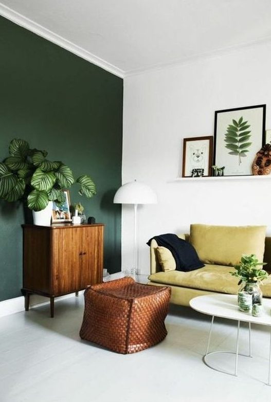 a boho living room with a dark green wall, a yellow sofa, potted plants and a gallery wall on a ledge