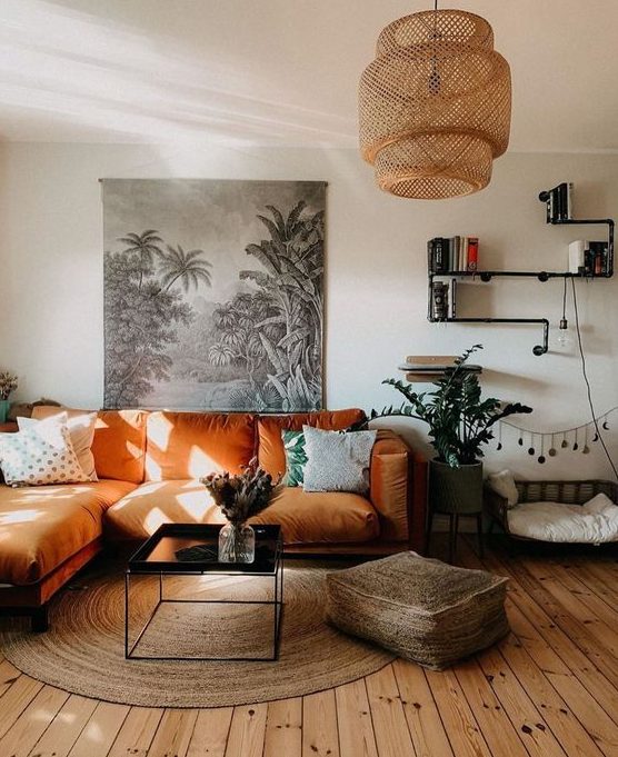 a boho living room with an orange sectional, a low table, a jute ottoman and a rug, a woven pendant lamp and potted plants