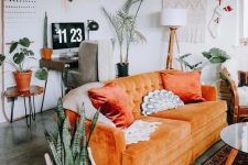 a boho living room with an orange sofa, potted plants, a macrame hanging, a small workspace in the corner is amazing