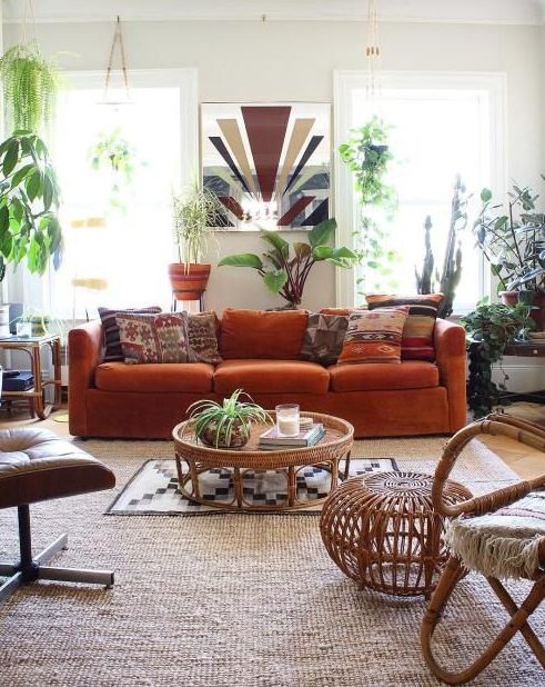 a boho living room with an orange velvet sofa as a centerpiece, potted plants and rattan and leather furniture, boho rugs