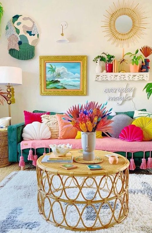 a boho maximalist living room with a green sofa, colorful pillows, rattan tables, bold artworks and a sunburst mirror and potted plants