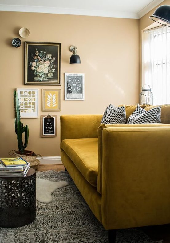 a boho nook with yellow walls, a mustard sofa, a gallery wlal and sconces and layered rugs plus a potted cactus