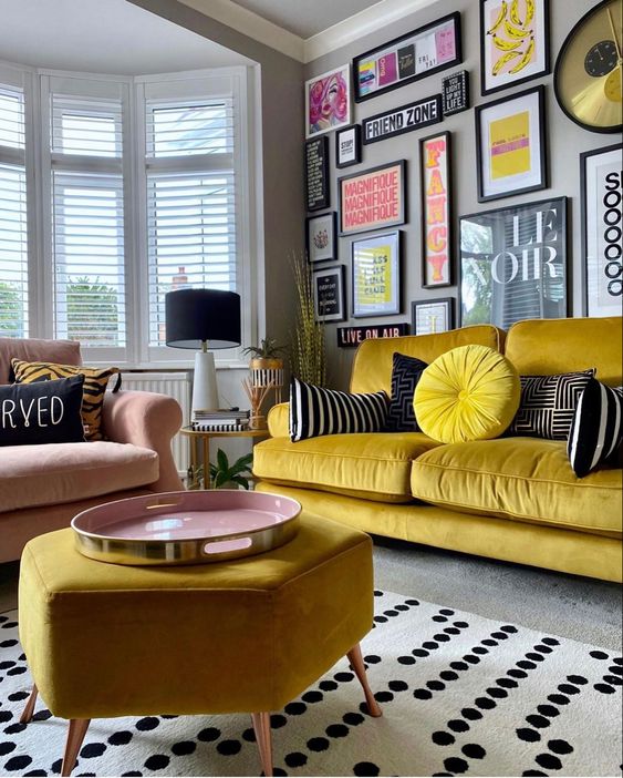 a bold and chic living room with grey walls, a yellow sofa and a pouf, a pink chair, a colorful gallery wall and a polka dot rug