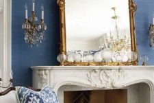 a bold and refined living room with blue grasscloth wallpaper, an antique fireplace, a mirror in an ornated frame, wall sconces and exquisite furniture