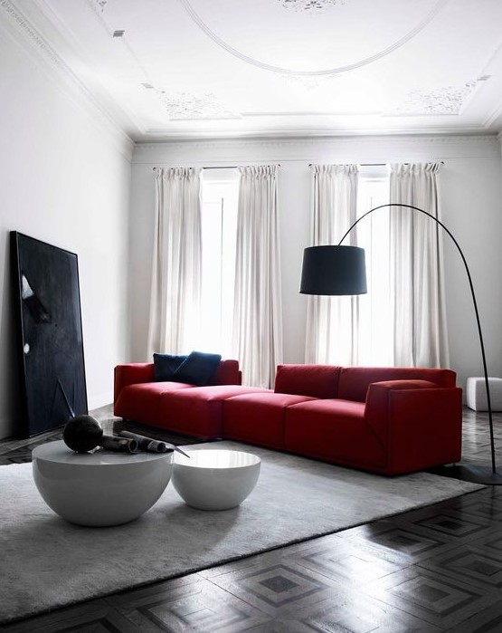 a bold contemporary living room with a large red sofa, a black artwork and a floor lamp and a duo of round tables